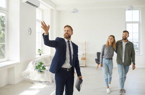 Real estate agent giving future tenants or first time buyers tour about modern spacious house. Boyfriend and girlfriend or husband and wife consider property investment, consult expert, buy new home
